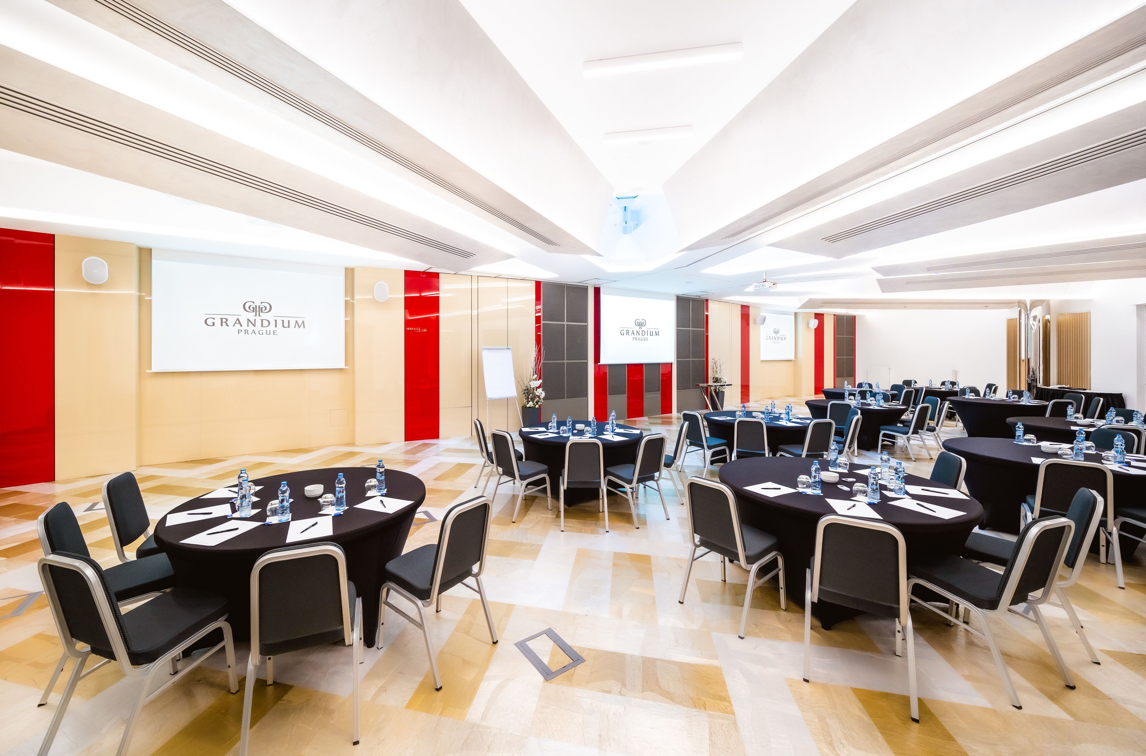 A conference room with multiple tables, chairs, and water bottles, featuring a modern design with red accents and a polished floor.