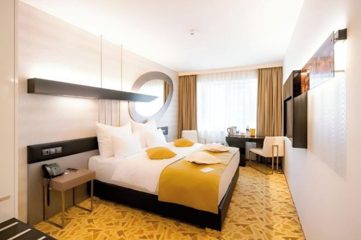 A hotel room with a bed, bedside table, chair, desk, and a TV.