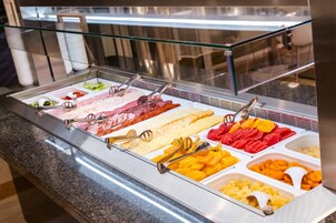 Buffet com diversos alimentos, incluindo carnes, queijos, frutas e legumes.