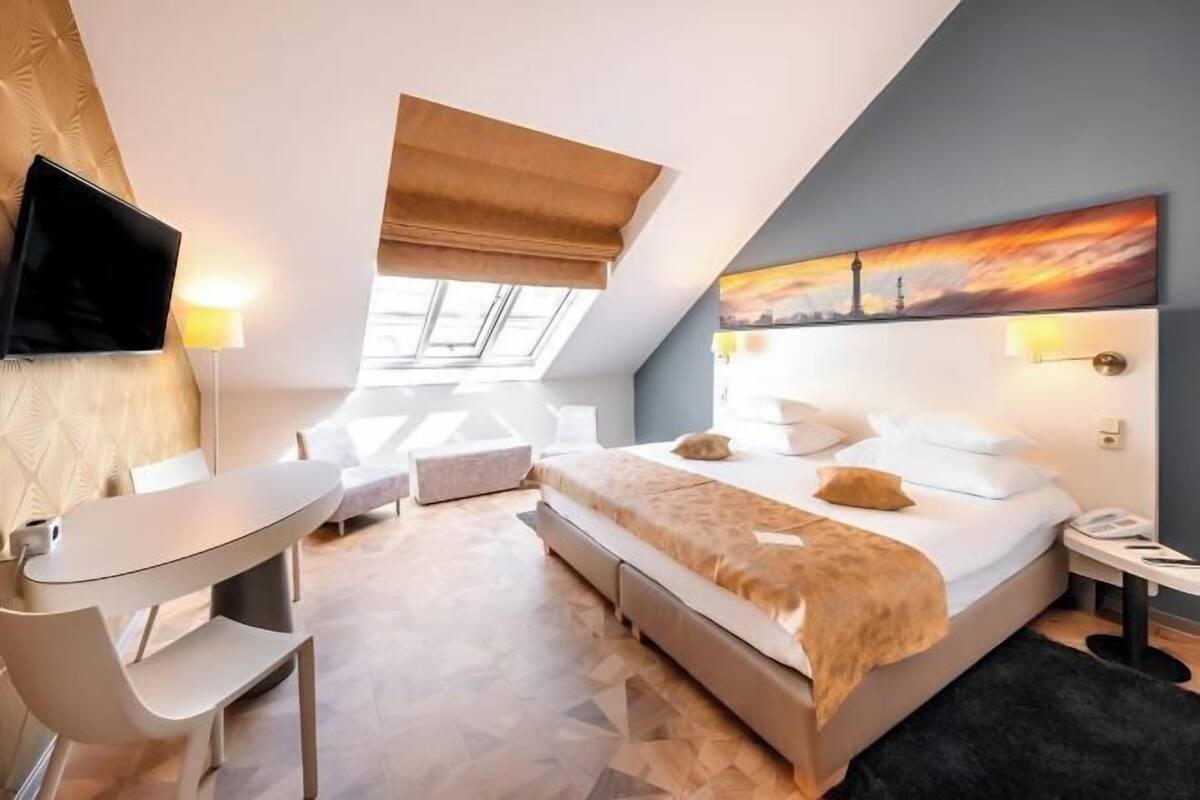 Ein modernes Hotelzimmer mit Bett, Schreibtisch, Sessel, Fernseher und einem Bild an der Wand.