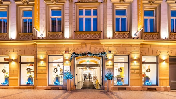 Une façade imposante d’hôtel, ornée de détails architecturaux raffinés, dotée de grandes fenêtres et d’une entrée centrale surmontée d’un arc décoratif.