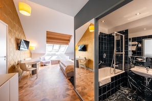 Una habitación de hotel moderna con una cama, mesita de noche y baño con ducha y lavabo.