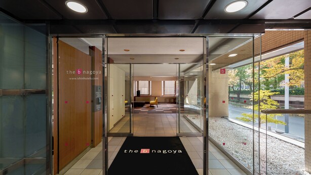 A hotel entrance with a glass door, a black mat with the hotel name, and a view of the interior and outside. - the b nagoya (Nagoya)