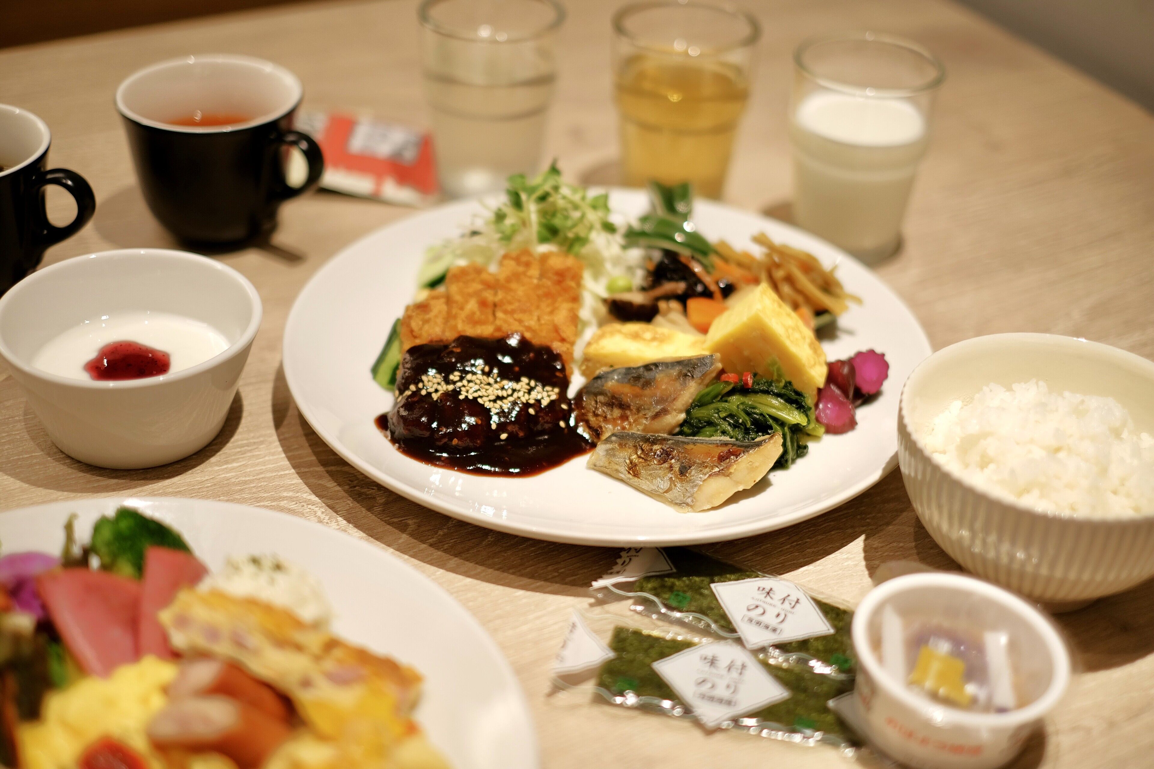 A table with various dishes, including sushi, rice, and a bowl of soup. There are also cups and glasses on the table.