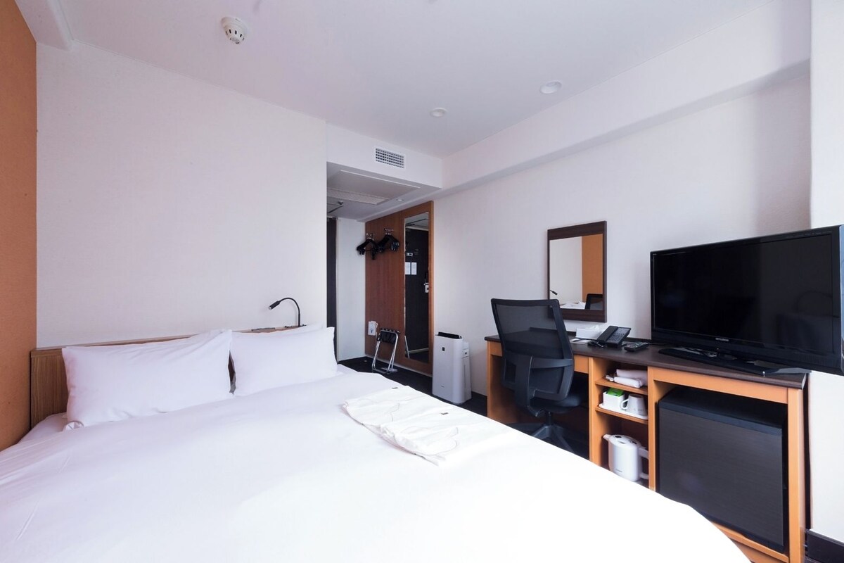 A hotel room with a bed, a desk with a computer, a television, and a mirror.