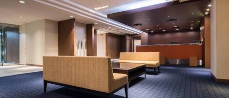 A hotel lobby with seating areas, a reception desk, and a patterned carpet.