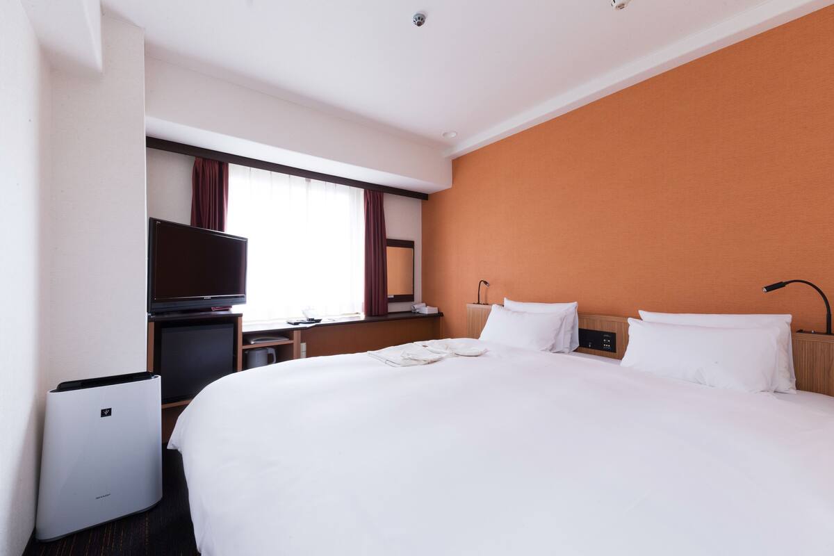 A hotel room with a large bed, a television, a desk, and a window with curtains.