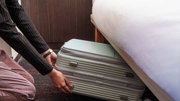 Une personne tenant une valise verte dans une pièce où se trouvent un lit et des meubles en bois.