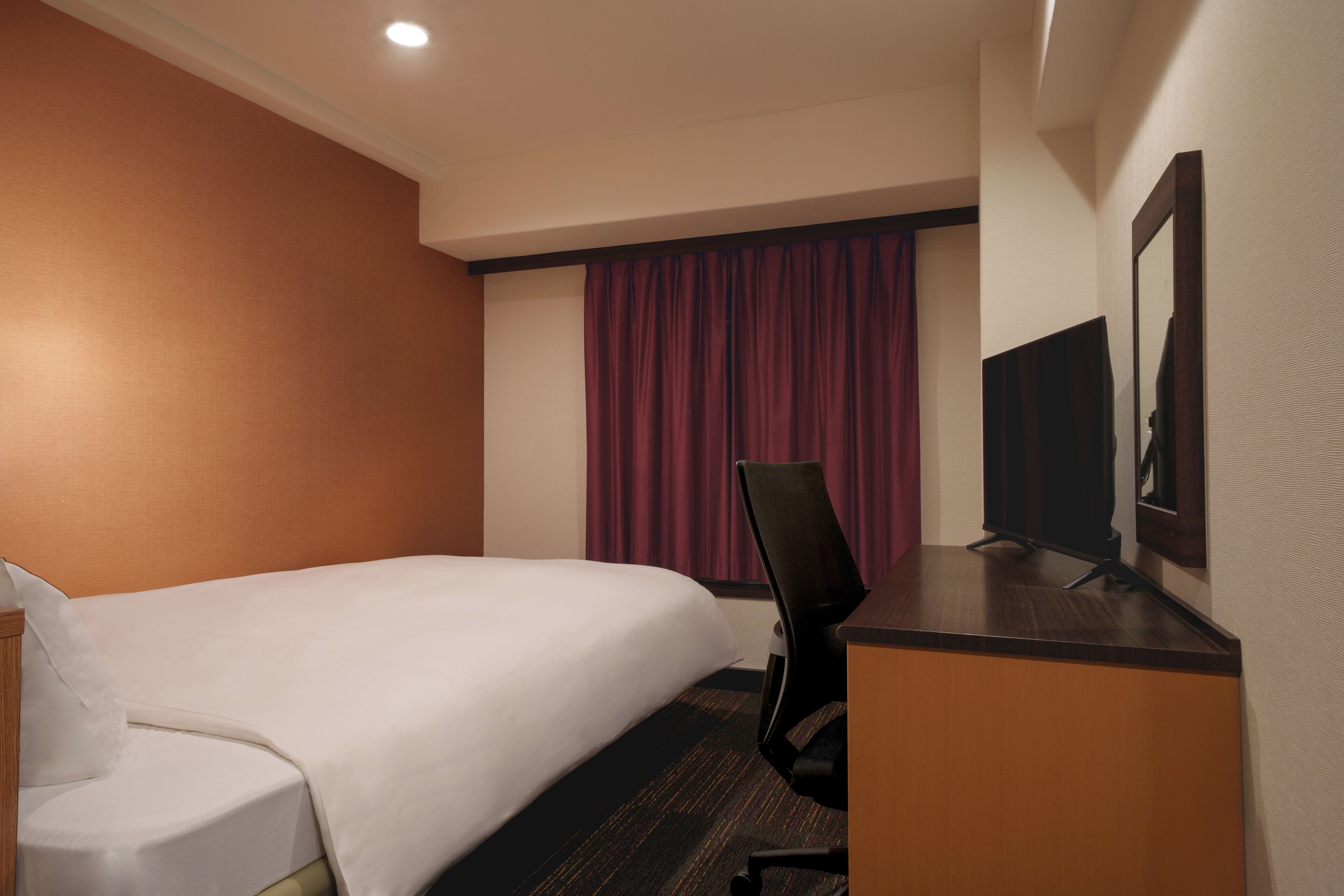 A hotel room with a bed, a desk, a chair, a television, and a window with curtains.
