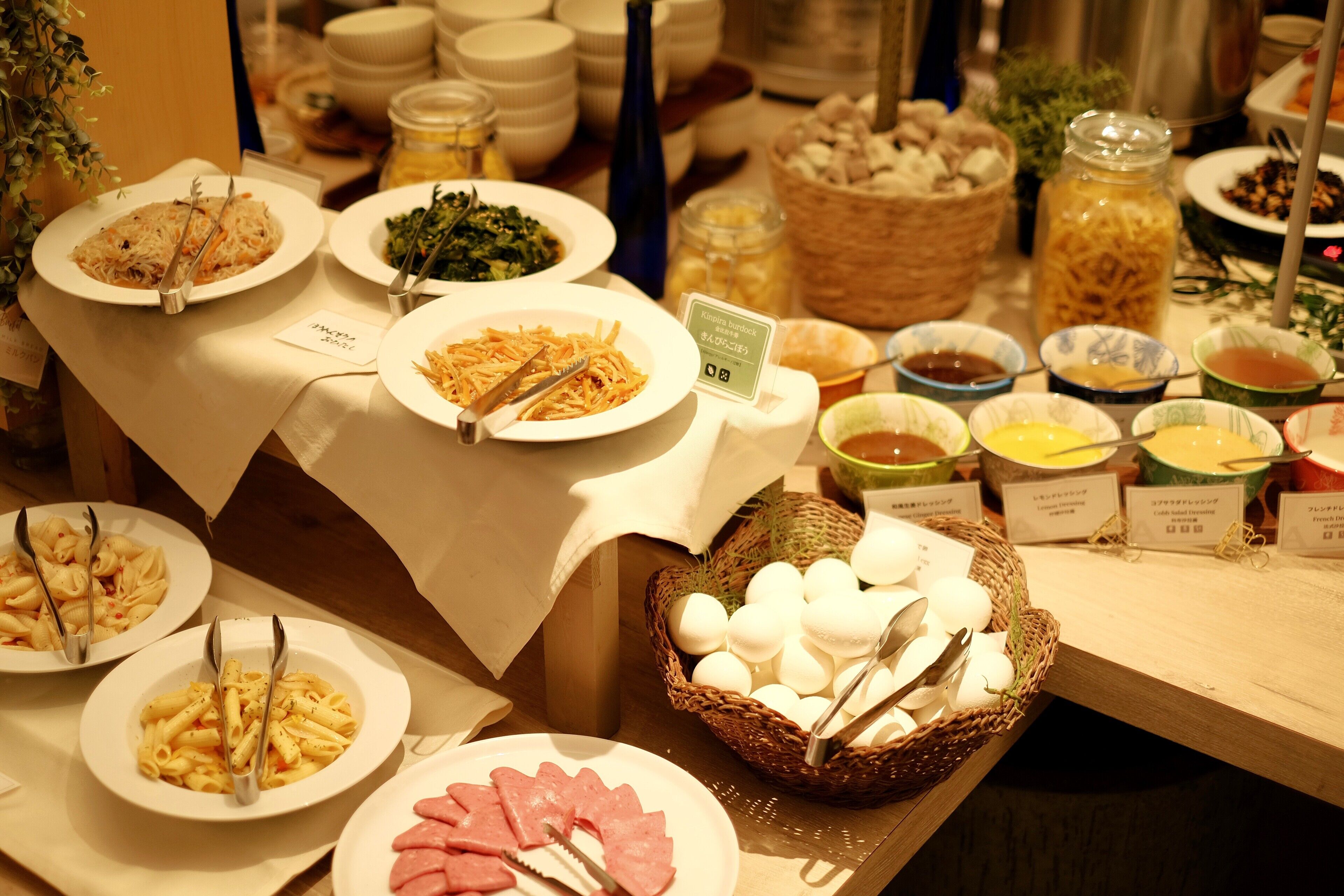 A buffet with various dishes including pasta, salads, and meats, with serving utensils and labels indicating the dishes.