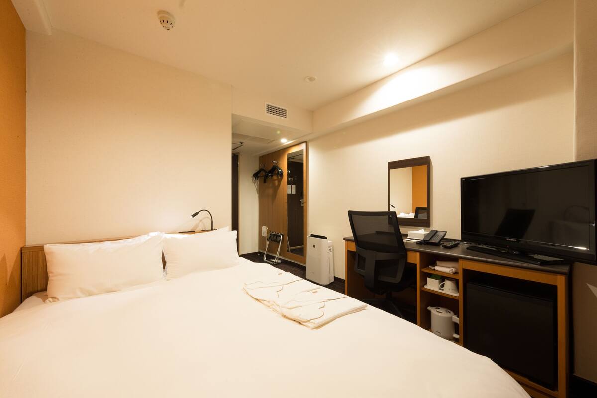 A hotel room with a bed, a desk with a computer, a television, and a mirror.