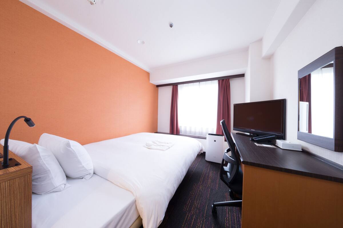 A hotel room with a bed, a desk, a TV, and a large window with curtains.