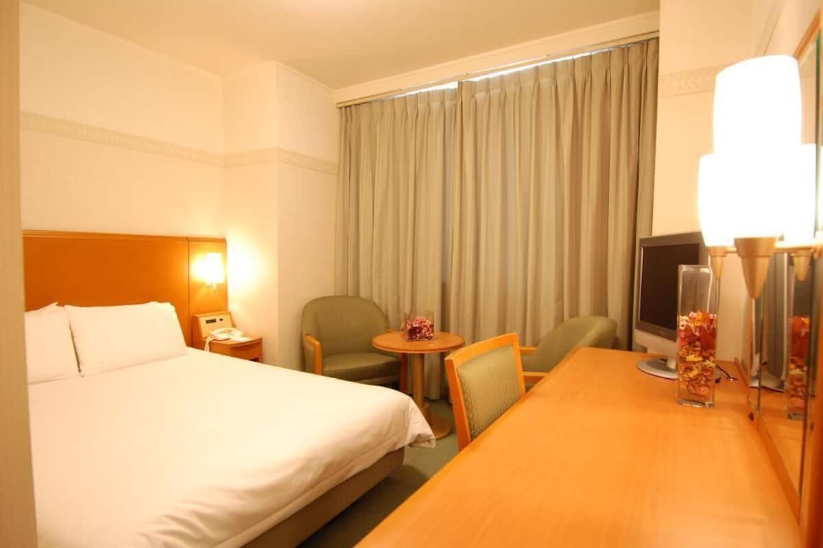 Ein Hotelzimmer mit einem großen Bett, einem Schreibtisch, einem Stuhl, einem Fernseher und einem Fenster mit Vorhängen.