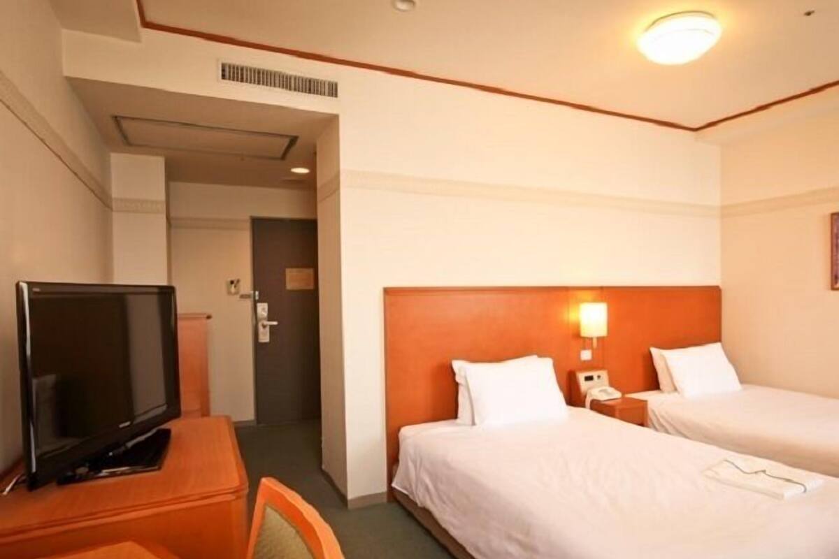 Ein Hotelzimmer mit zwei Betten, einem Fernseher, einem Schreibtisch und einem Sessel.