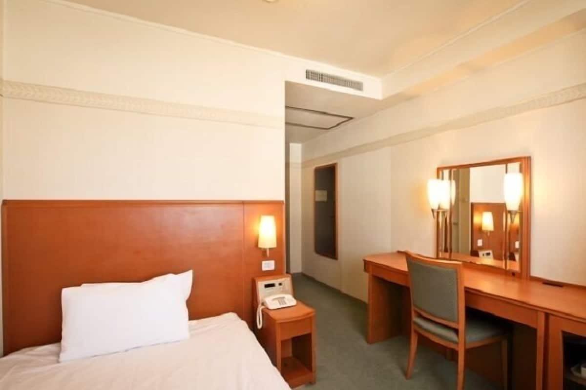 Ein Hotelzimmer mit Bett, Nachttisch mit Telefon, Schreibtisch mit Stuhl und Spiegel.