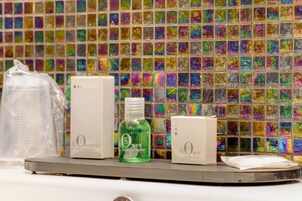 Un bagno con una parete rivestita da mosaici colorati, una bottiglia di shampoo e due confezioni di gel doccia.
