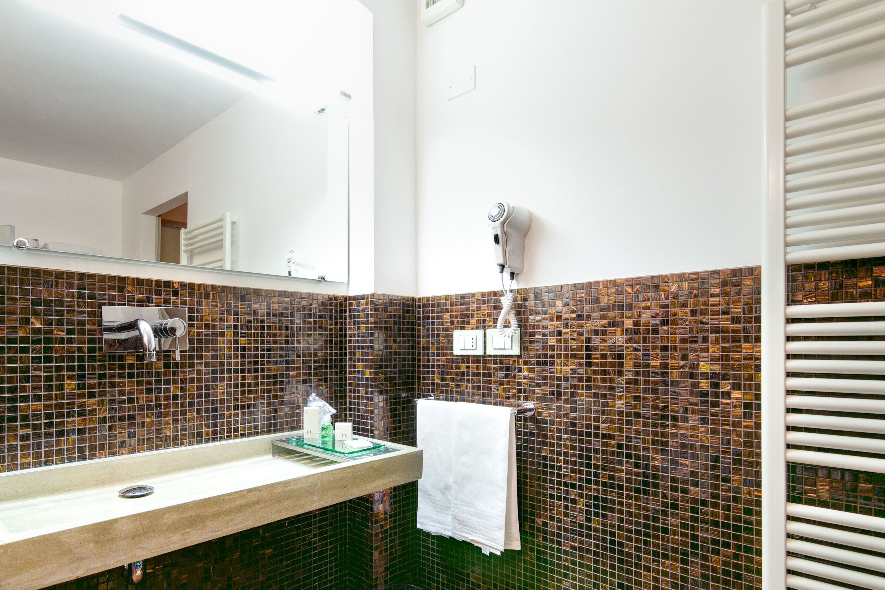 Un baño con salpicadero de azulejos, un espejo, un perchero para toallas y un secador de pelo montado en la pared.
