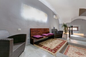 Un intérieur moderne avec un plafond haut, un lit doté d’une tête de lit en bois, une chaise en osier, une plante en pot et un tapis à motifs.