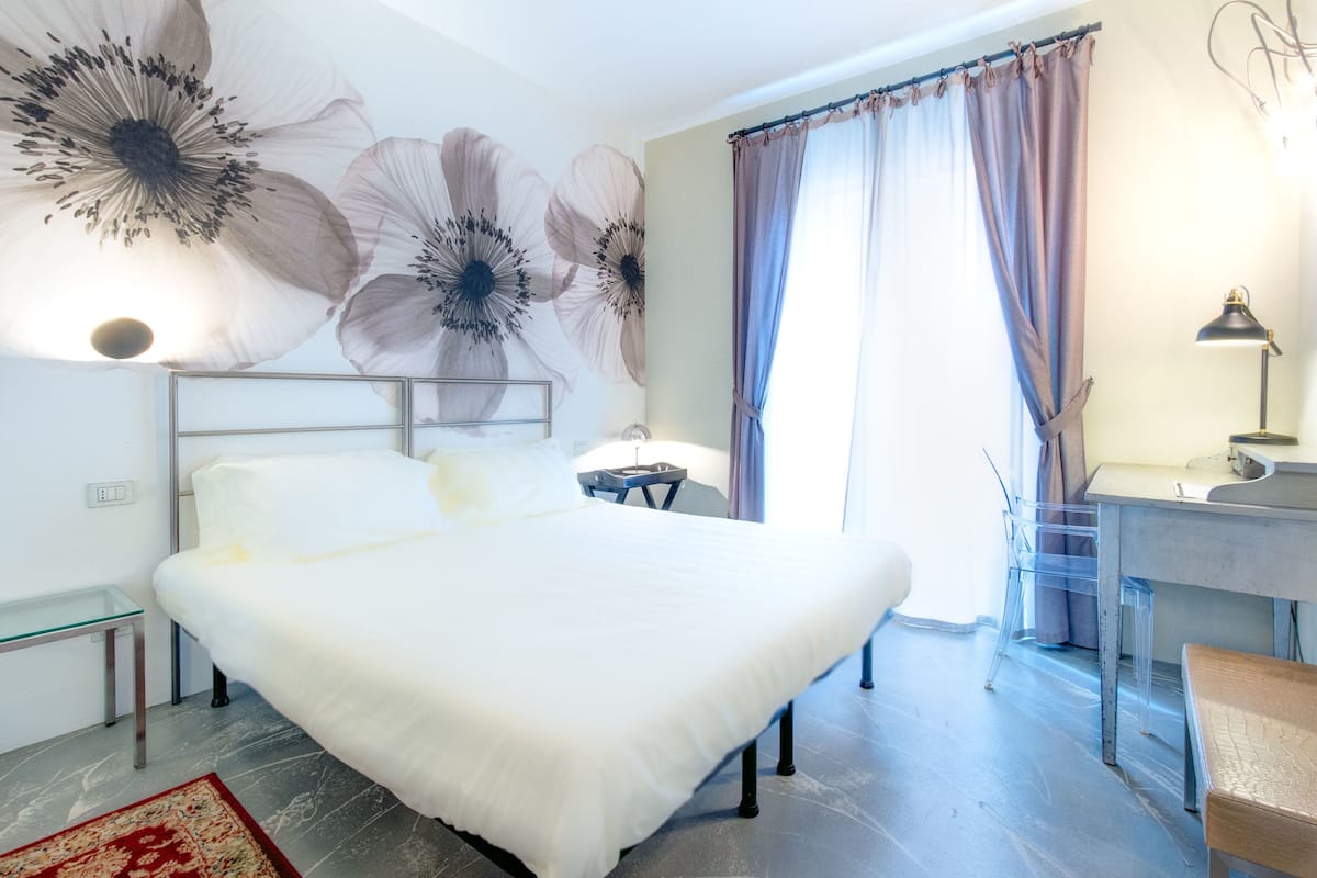 Un dormitorio con una cama grande, un escritorio, una silla y un cuadro floral en la pared.