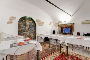 Een eetgedeelte met tafels gedekt voor een maaltijd, een groot schilderij aan de muur en een vloerkleed met een patroon.