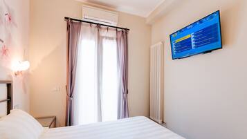 A hotel room with a bed, a wall-mounted TV displaying a menu, a window with curtains, and a radiator.