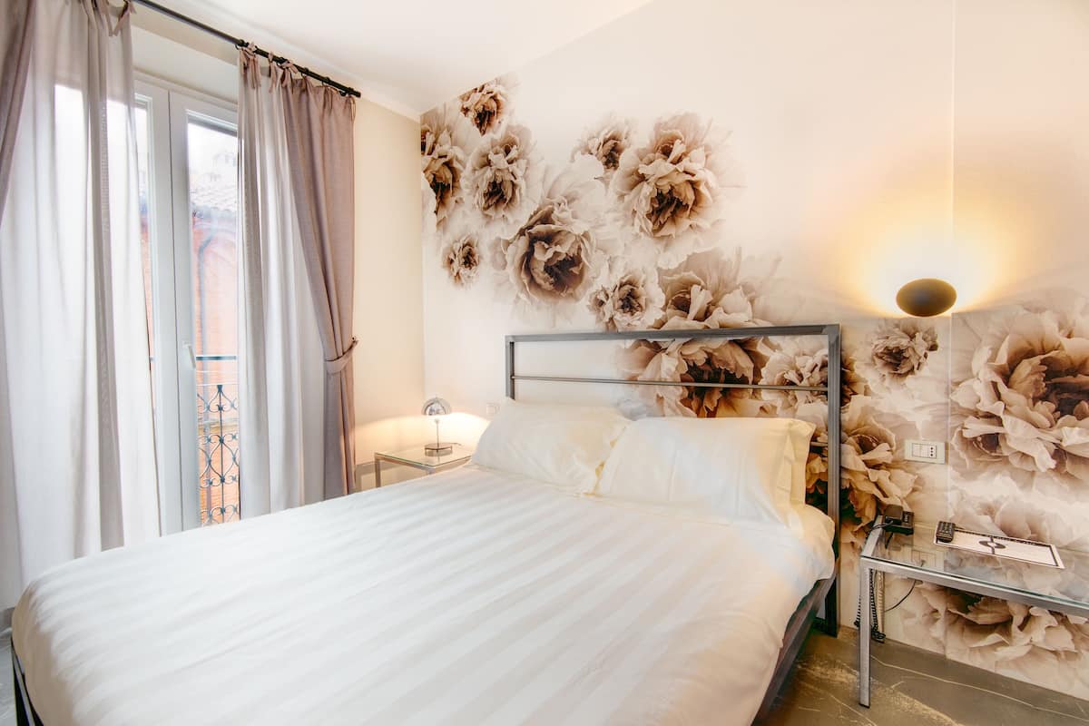 Una habitación de hotel con una cama, una mesita de noche, una lámpara y un papel tapiz floral.