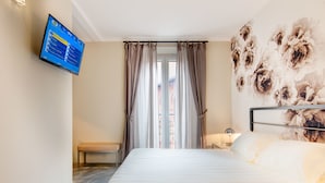 Habitación de hotel con cama, escritorio, silla, televisor montado en la pared y ventana con cortinas.
