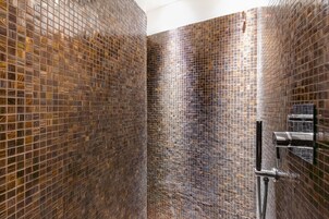 Un baño con paredes de mosaico y grifería de ducha cromada.