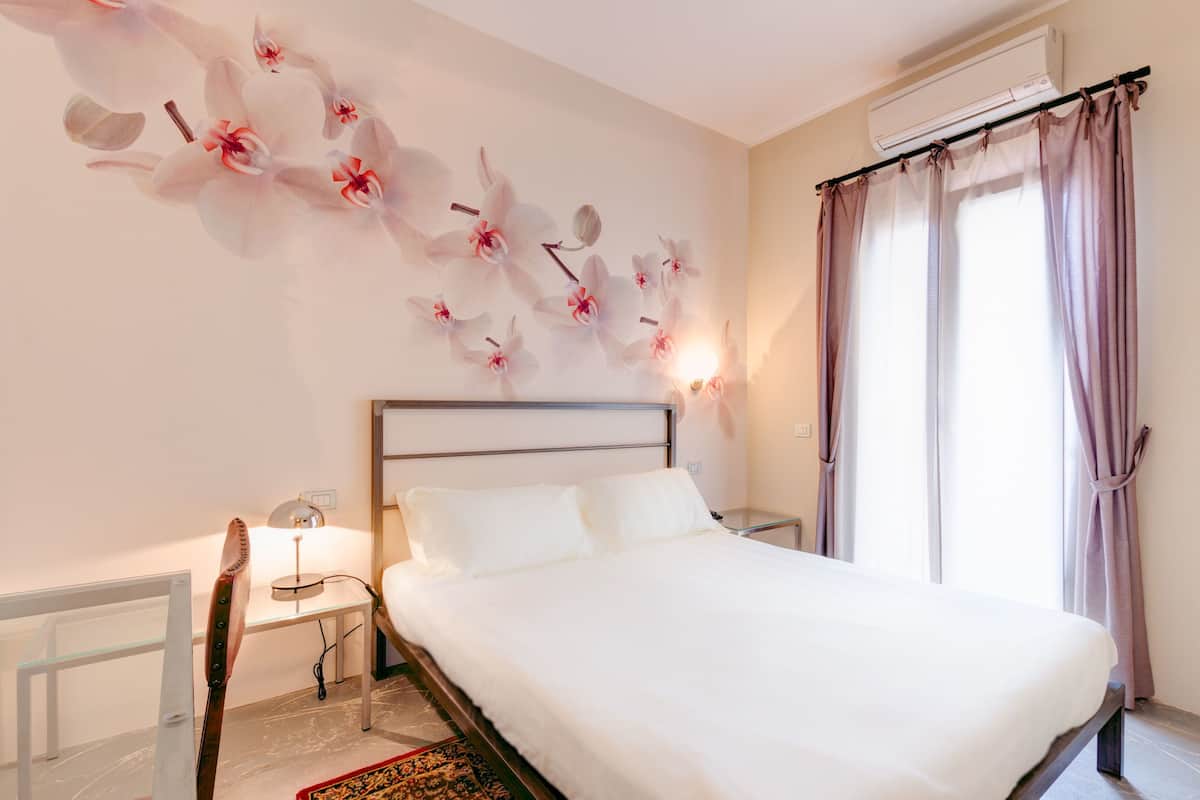 Un dormitorio con una cama, una mesita de noche, una lámpara y una pared con un mural floral.
