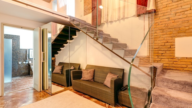 Un interior moderno con una escalera de cristal, un sofá de mimbre y vistas al exterior.