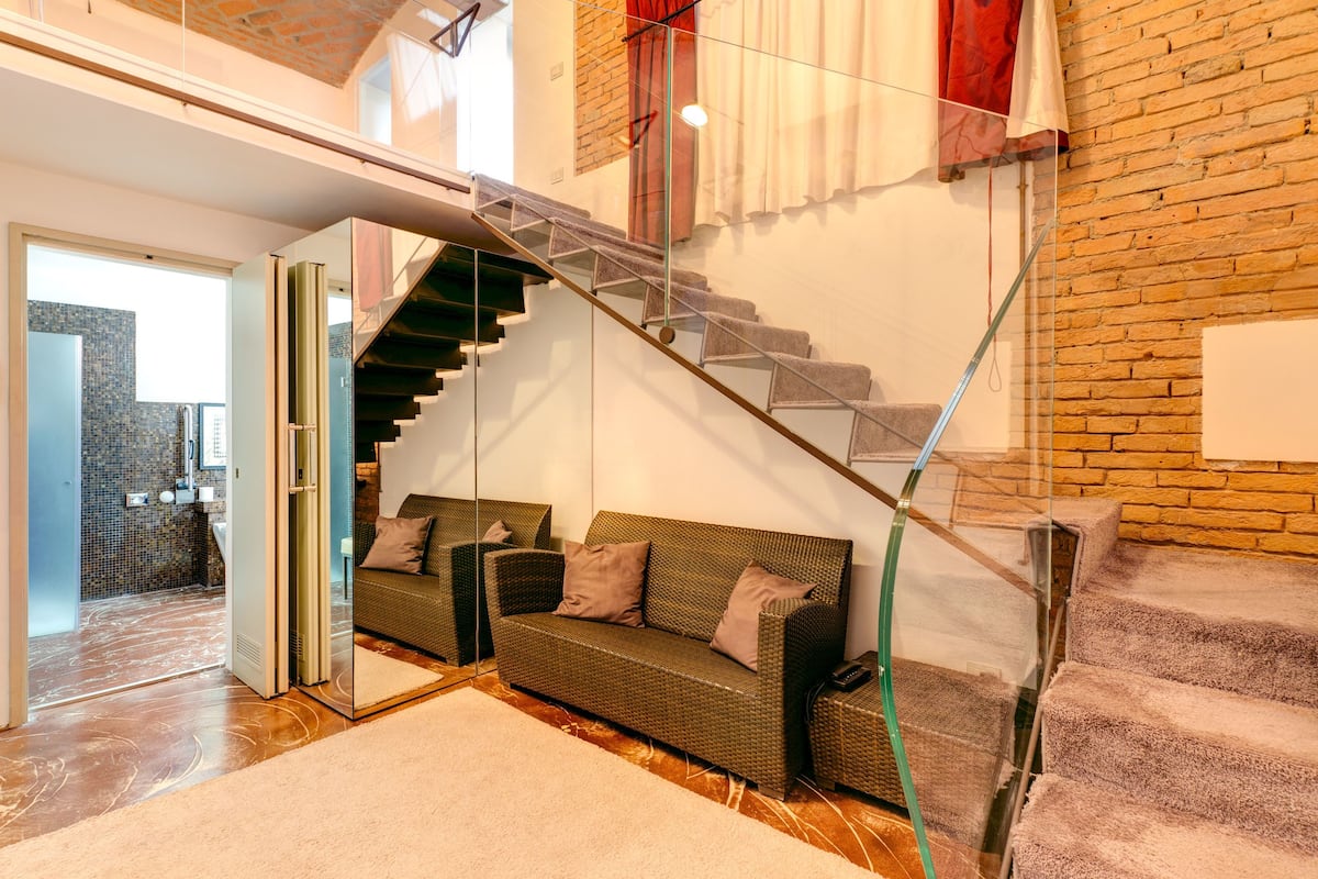 Un interior moderno con una escalera de cristal, un sofá de mimbre y vistas al exterior.