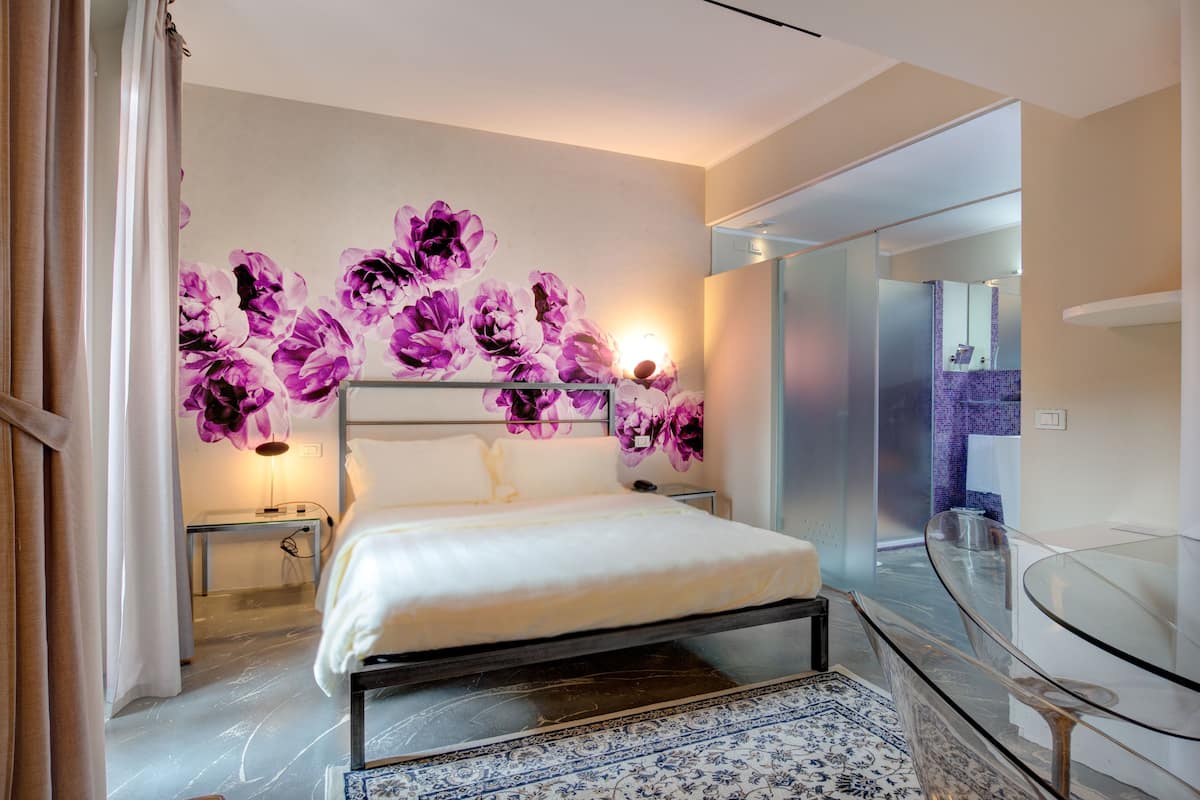 Un dormitorio moderno con una cama grande, un balcón con cerramiento de vidrio y un mural floral decorativo.