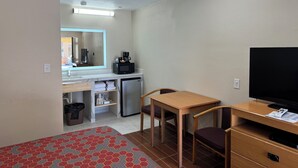 A compact hotel room with a bed, a desk, a chair, a television, a microwave, a refrigerator, and a ceiling fan. - Townhouse Inn & Suites (Brawley)