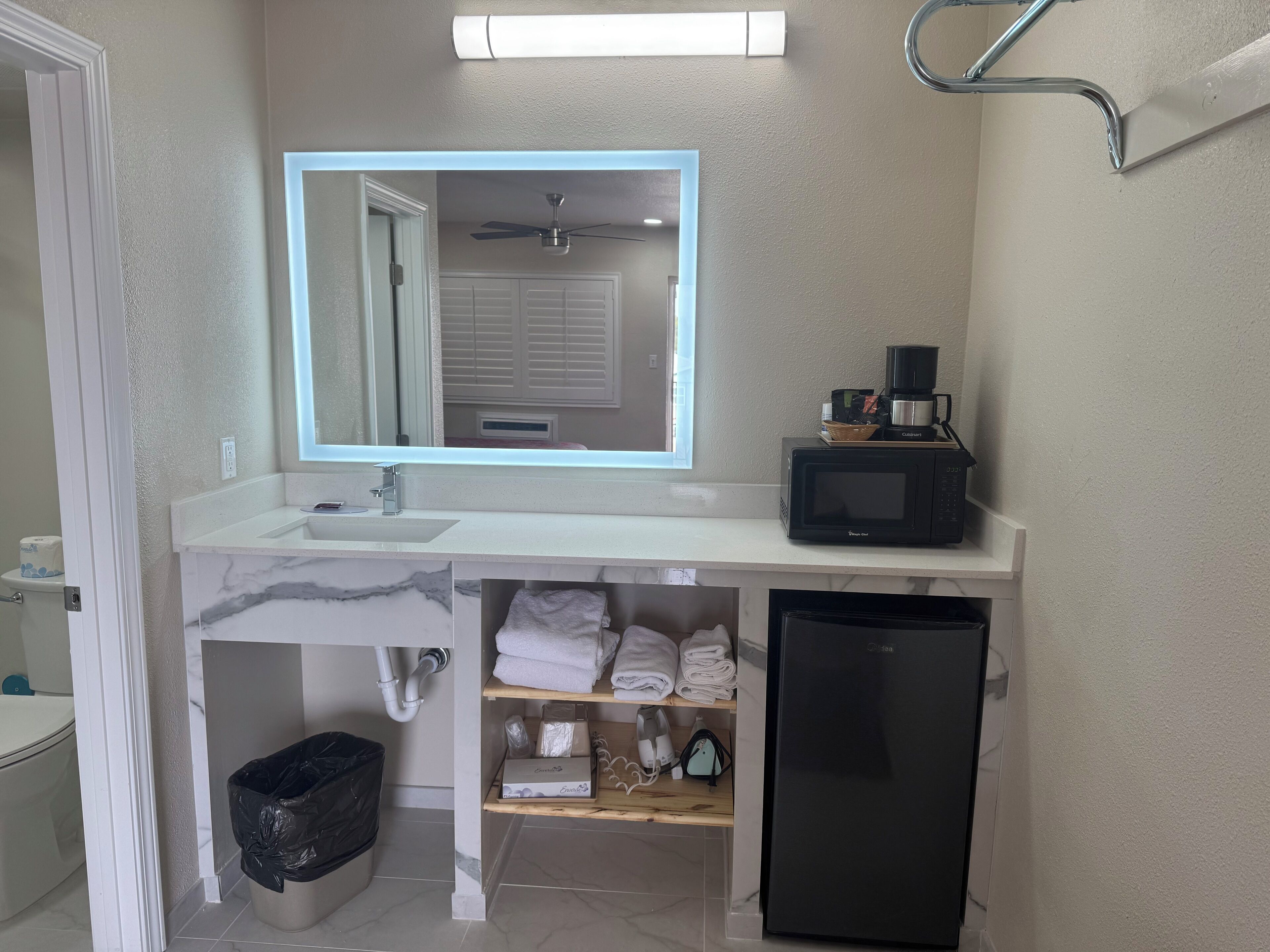Un baño con tocador blanco, microondas negro, cubo de basura negro y refrigerador negro.