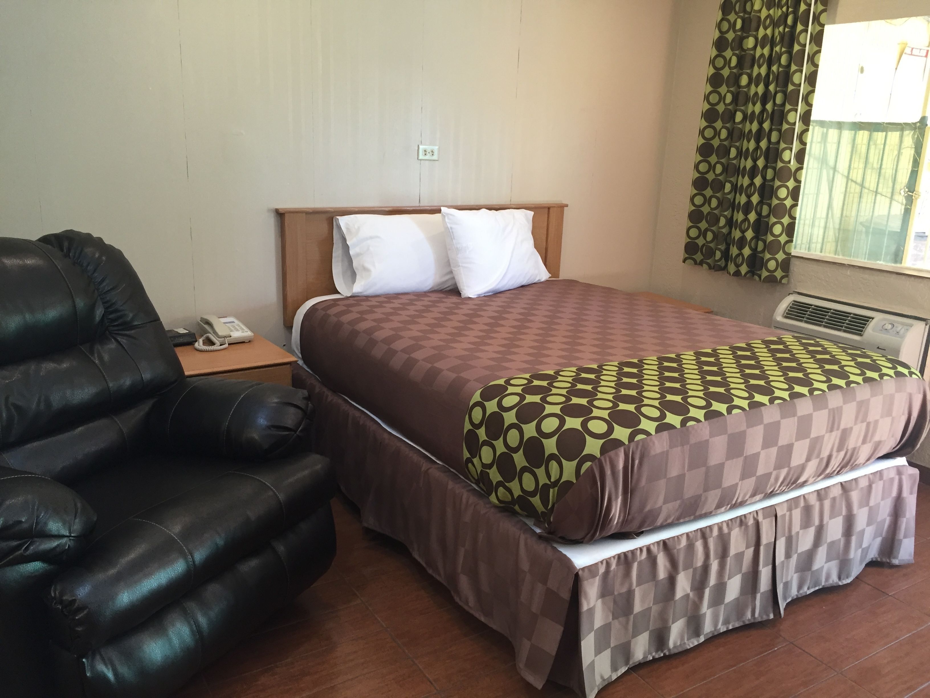 Une chambre d’hôtel avec un lit, un canapé en cuir, une table de chevet avec un téléphone et une fenêtre avec des rideaux.