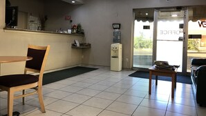 A reception area with a wooden chair, a small table, a water dispenser, and a ceiling fan. - Townhouse Inn & Suites (Brawley)