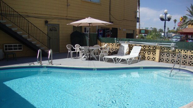 A swimming pool with lounge chairs and an umbrella, surrounded by a fence and a building with a staircase. - Townhouse Inn & Suites (Brawley)
