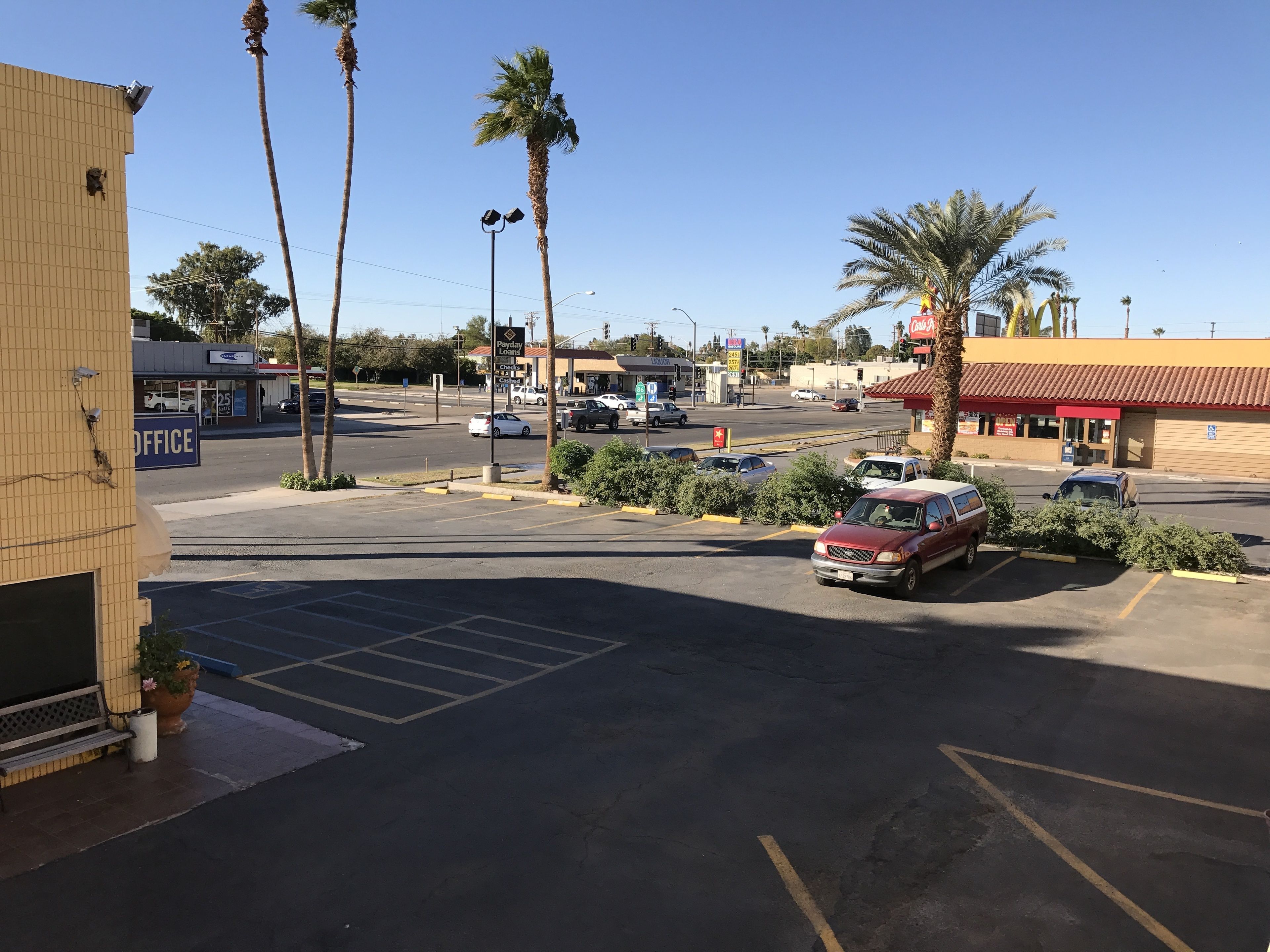 Un estacionamiento con un coche rojo, palmeras y un edificio con un letrero de 'Payday Loans'.