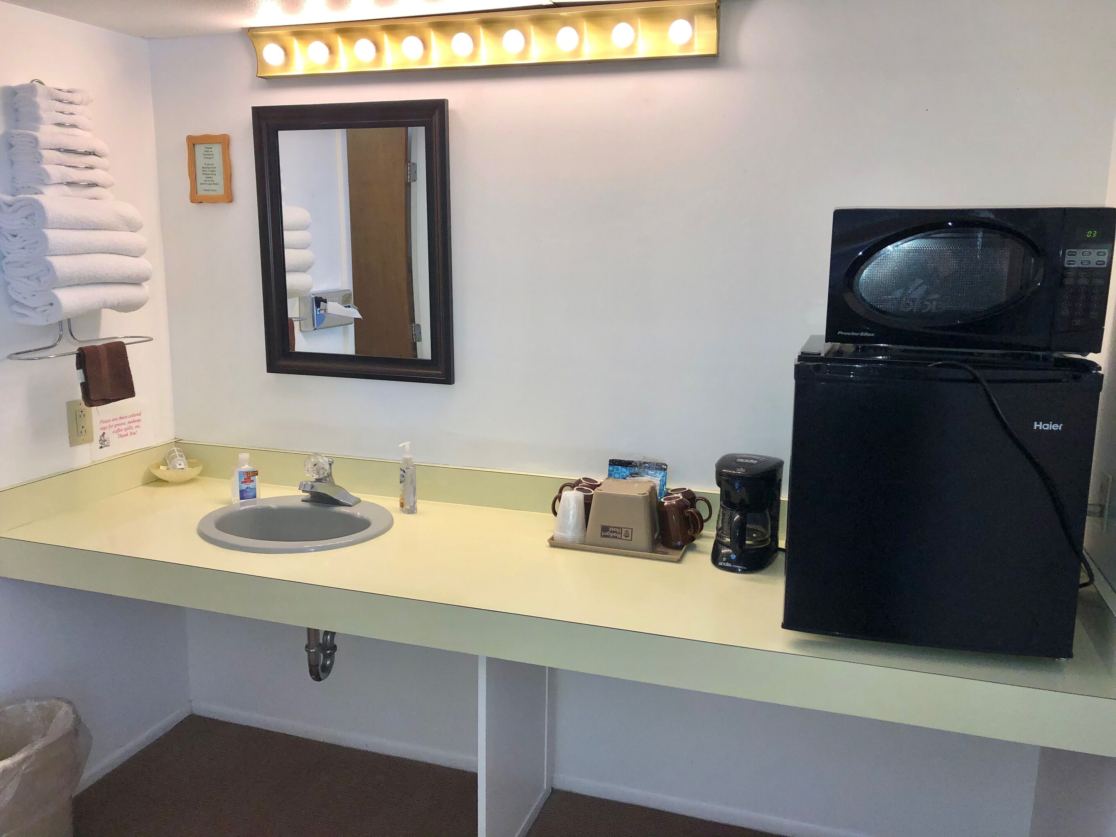 Une salle de bain d’hôtel équipée d’un lavabo, d’un miroir, d’un porte-serviettes et d’un réfrigérateur noir de la marque Haier.
