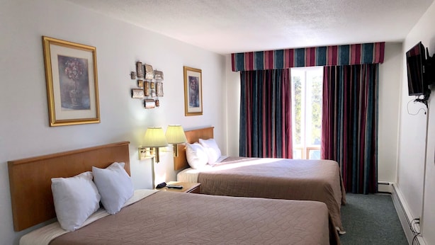A hotel room with two beds, a nightstand, lamps, a TV, and a window with curtains.
