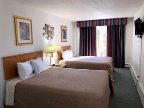 Habitación de hotel con dos camas, una mesita de noche, lámparas, televisor y ventana con cortinas.