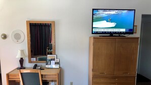 A hotel room with a wooden desk, chair, and a television displaying a news broadcast.