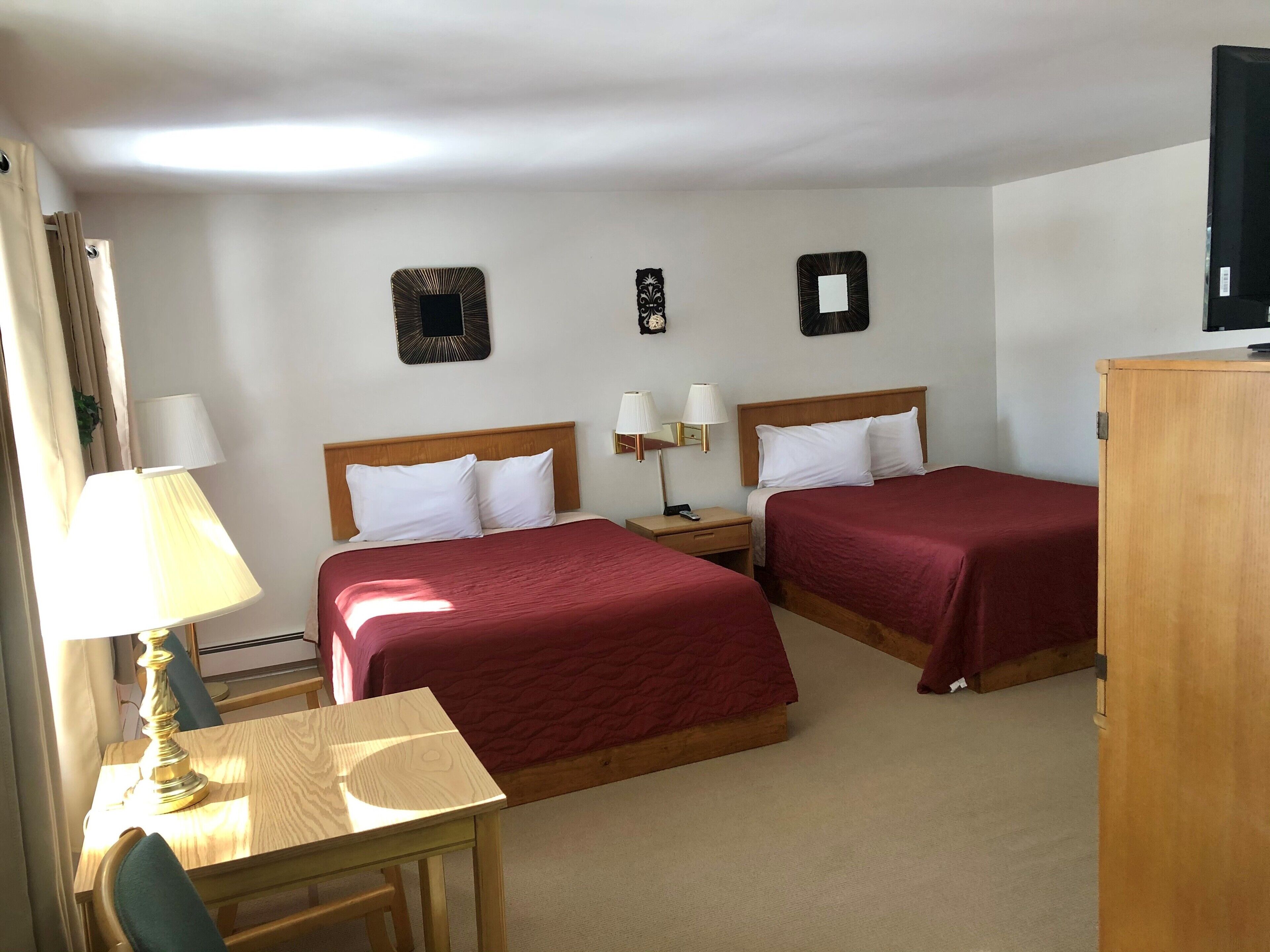 Una habitación de hotel con dos camas, un escritorio, una lámpara y un televisor.