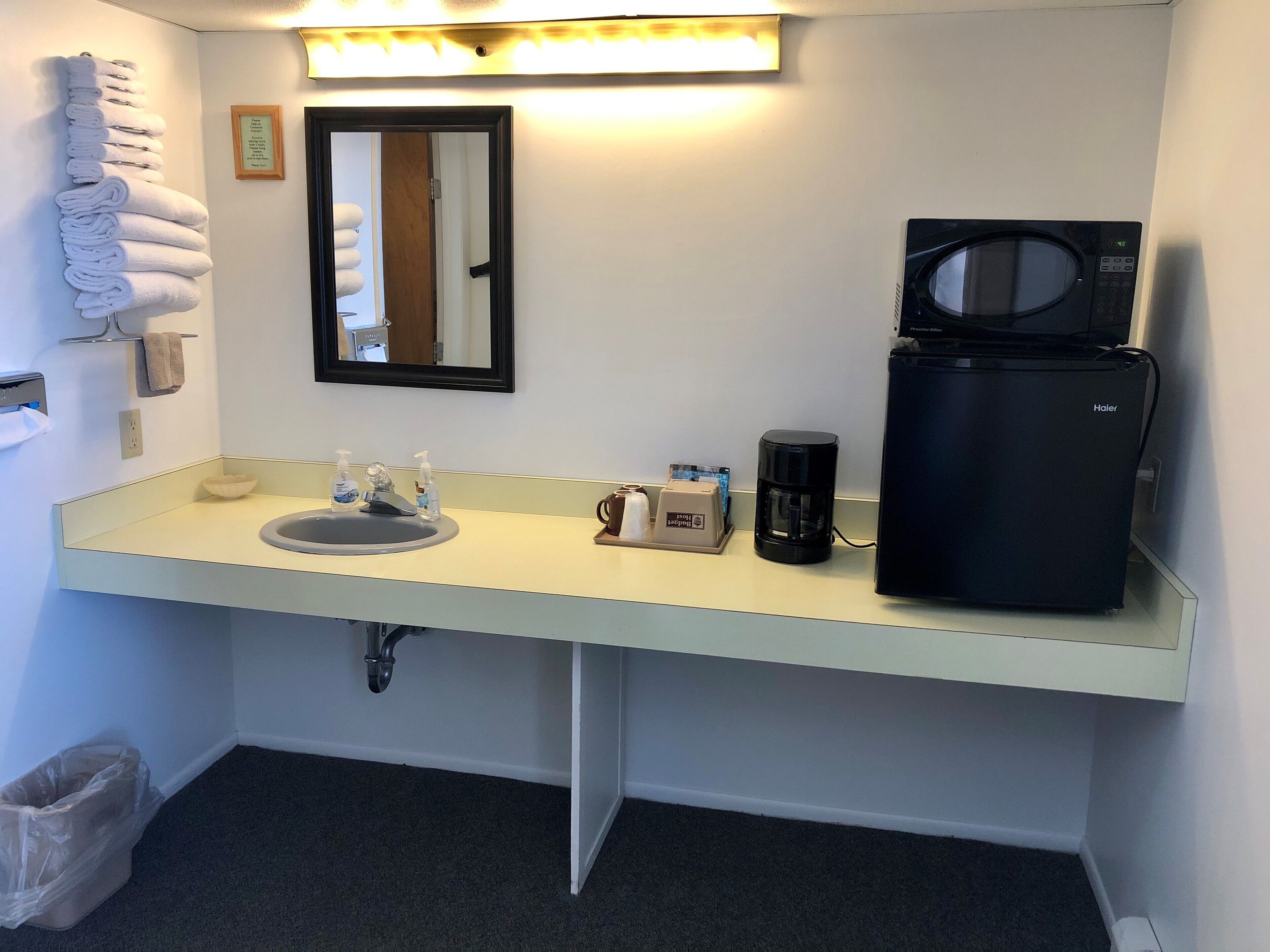 A hotel bathroom with a sink, mirror, towel rack, and a coffee maker.