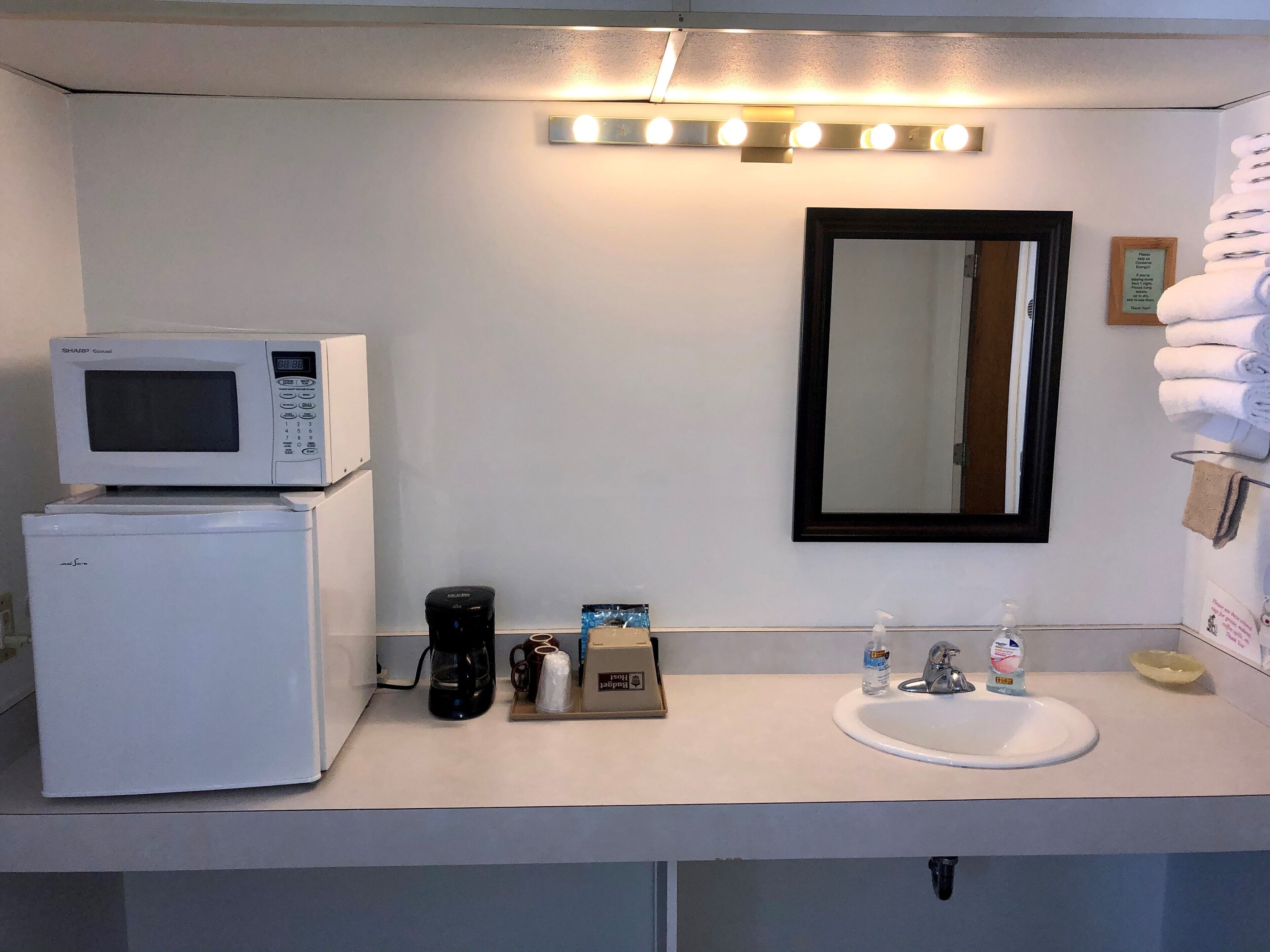 Ein kleines Badezimmer mit Waschbecken, Spiegel, Mikrowelle und Kaffeemaschine.