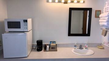 Ein kleines Badezimmer mit Waschbecken, Spiegel, Mikrowelle und Kaffeemaschine.
