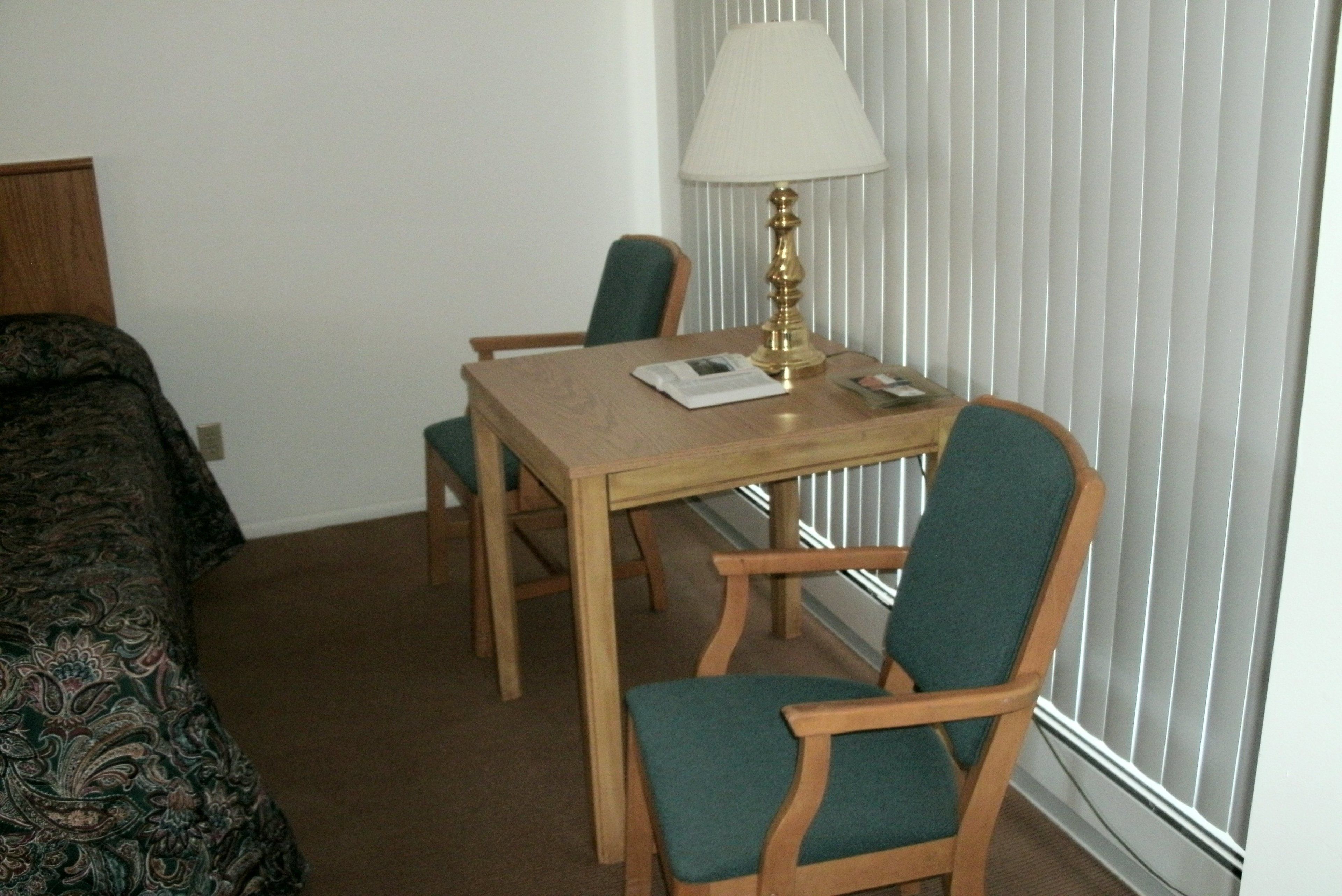 Habitación de hotel con una mesa de madera, dos sillas, una lámpara y una cama con cubrecama estampado.