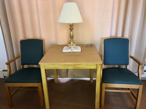 Una habitación con una mesa de madera, dos sillones tapizados en azul, una lámpara y un libro sobre la mesa.
