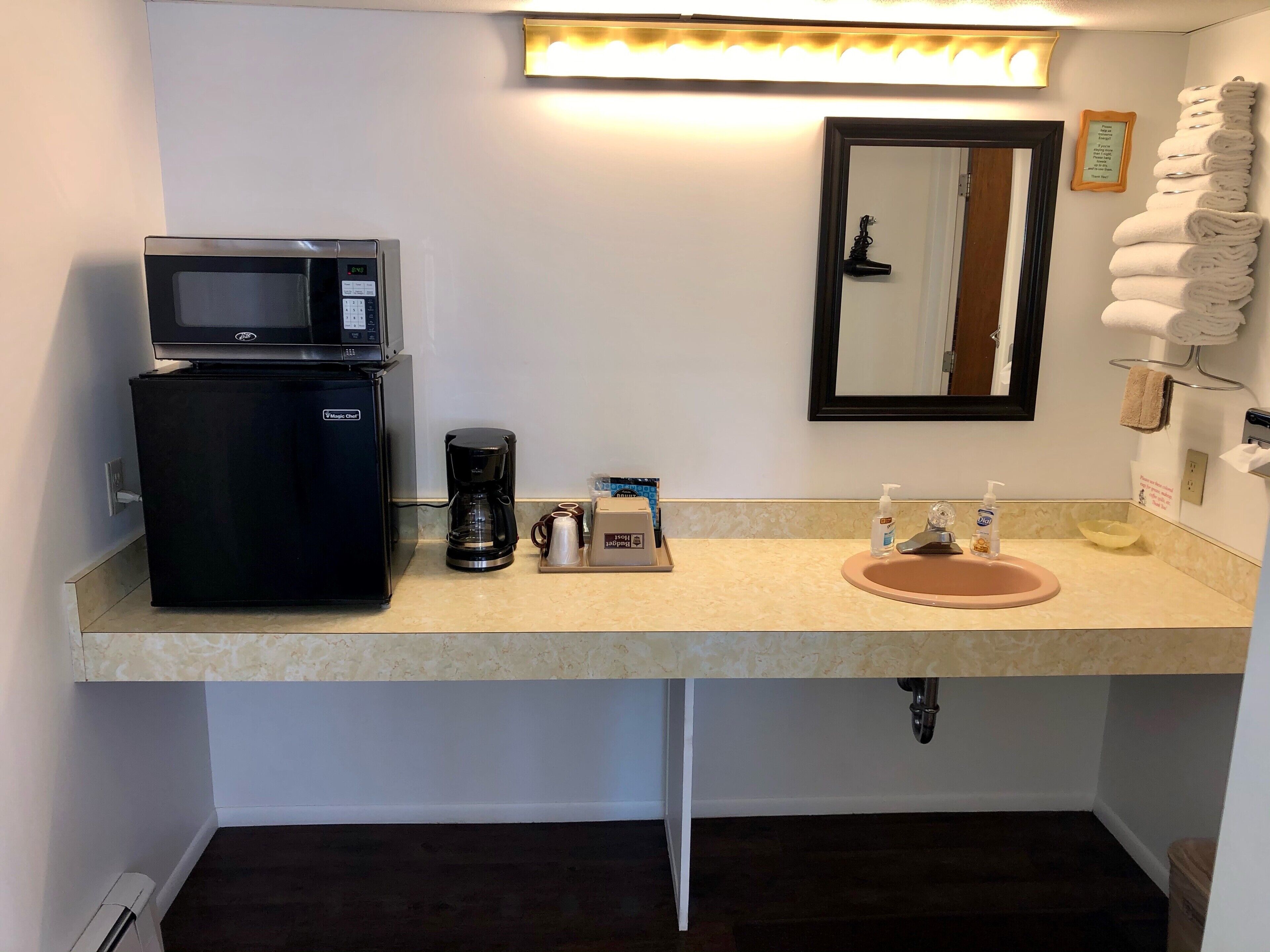 Un baño de hotel con lavamanos, espejo, toallero y un refrigerador con microondas.