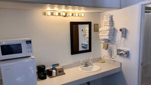 A hotel bathroom with a white sink, a microwave, a coffee maker, and a hairdryer.